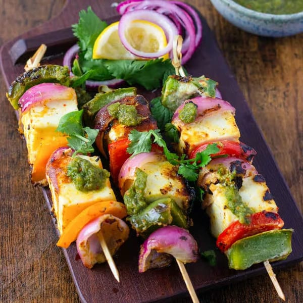 Three paneer tikka skewers with bell peppers and onions, garnished with cilantro and lemon.