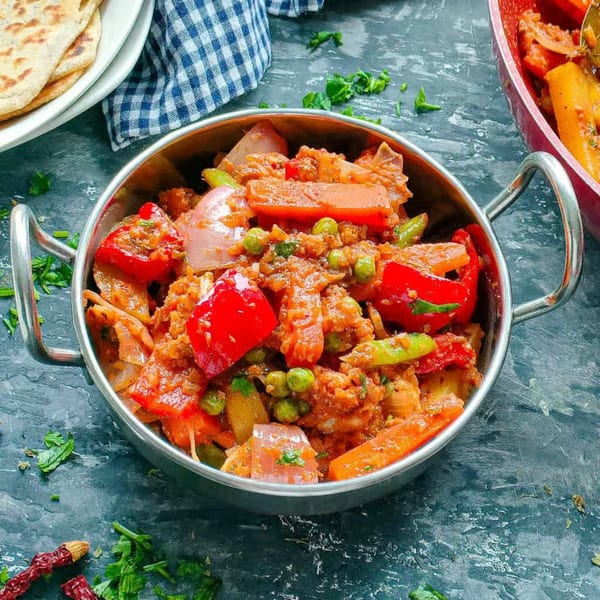A metal karahi bowl filled with colorful Indian vegetable curry, with flatbreads in the background.
