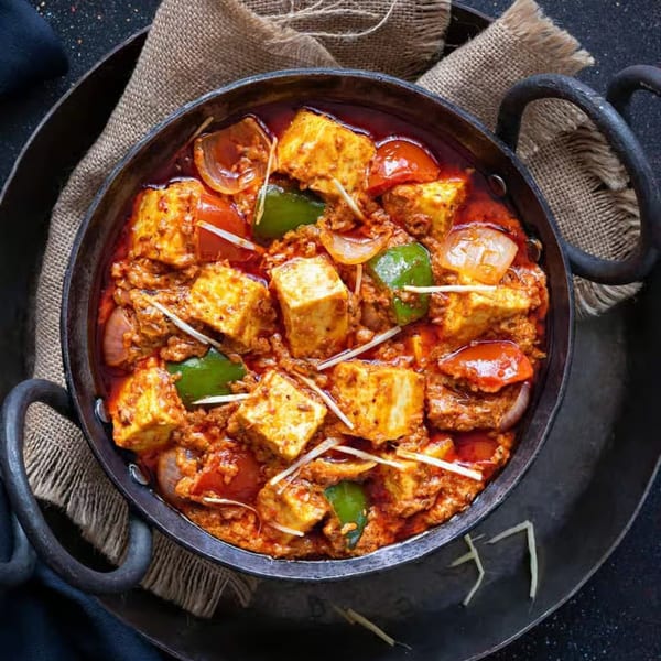 Indian paneer curry with bell peppers, onions, and ginger in a black cast iron pot.