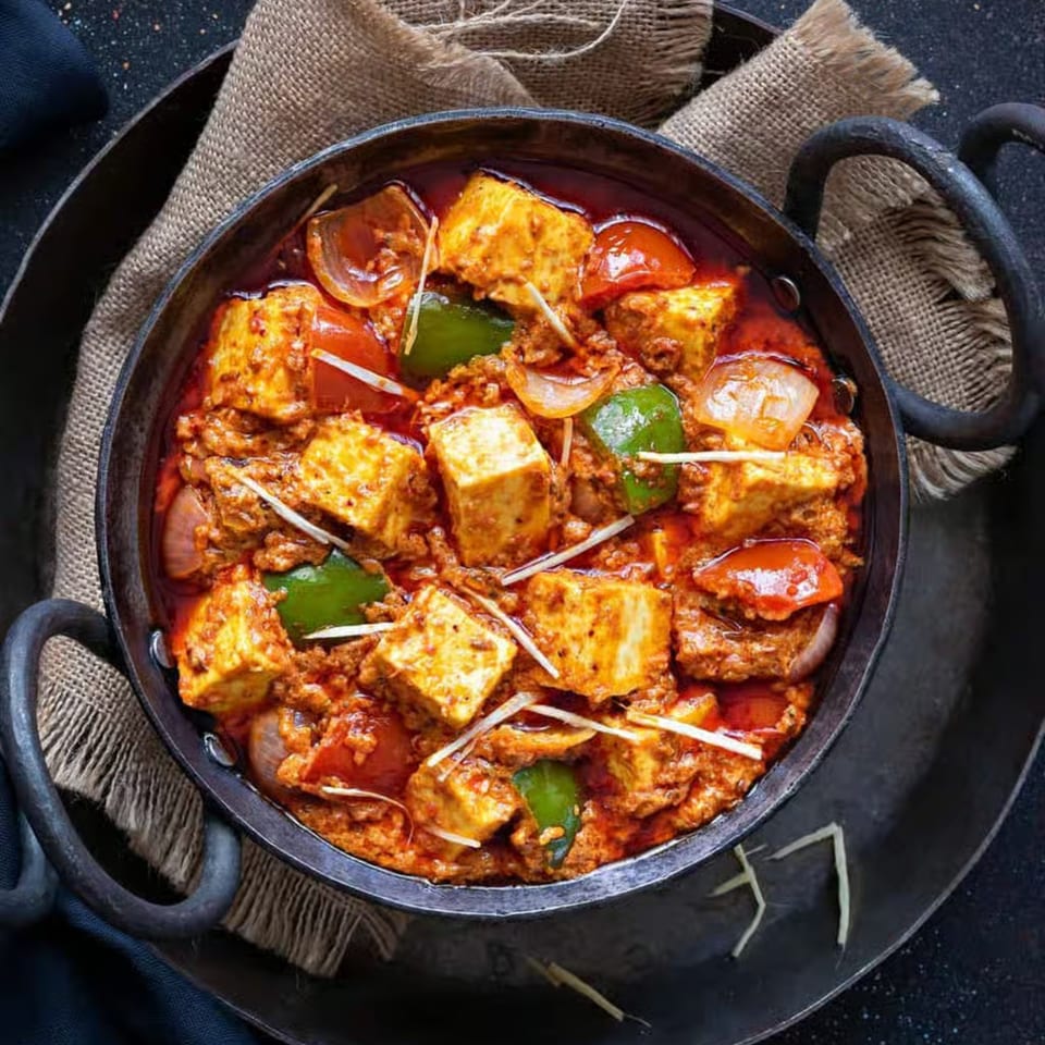 Indian paneer curry with bell peppers, onions, and ginger in a black cast iron pot.