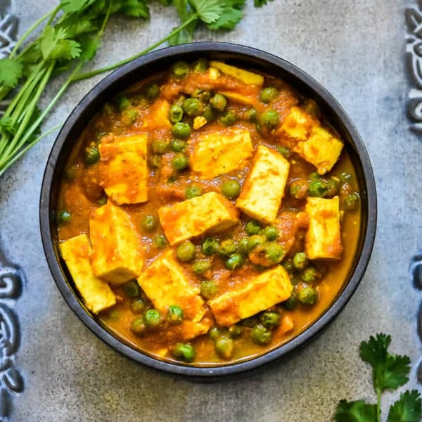 A black bowl of vibrant orange Mutter Paneer, an Indian dish with peas and paneer cheese, garnished with cilantro.