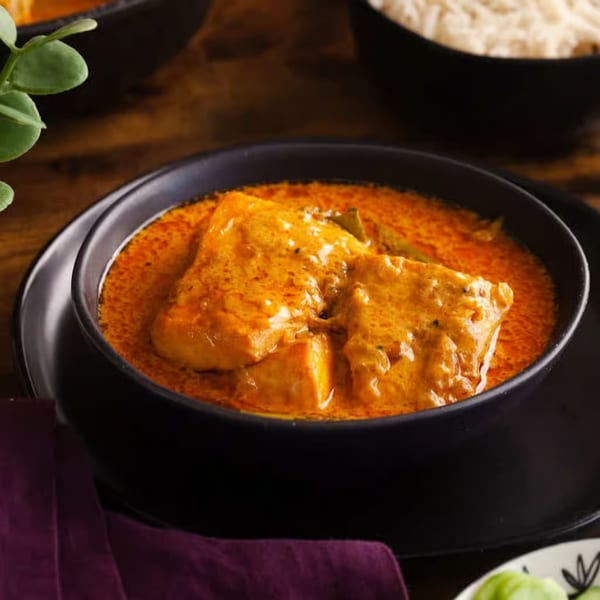 Indian fish curry in a black bowl, with rice and a purple napkin in the background.