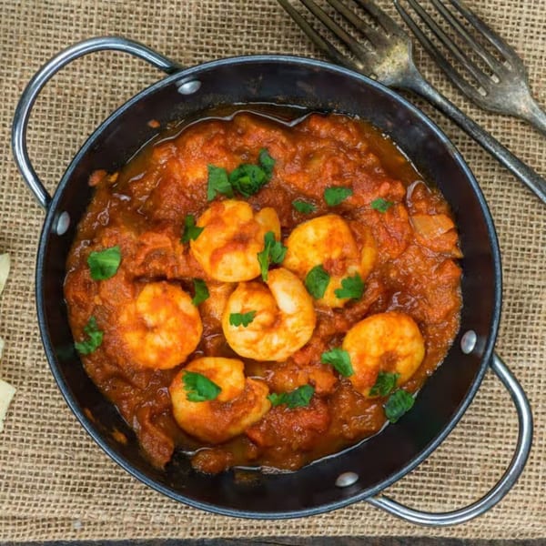 Indian shrimp curry in a black pan, garnished with cilantro, on a burlap surface.
