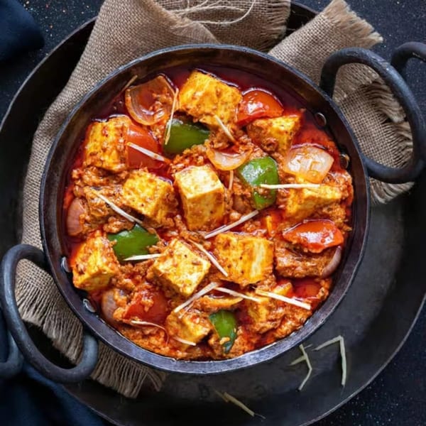 A cast iron pan filled with paneer tikka masala, garnished with ginger, on a burlap cloth.