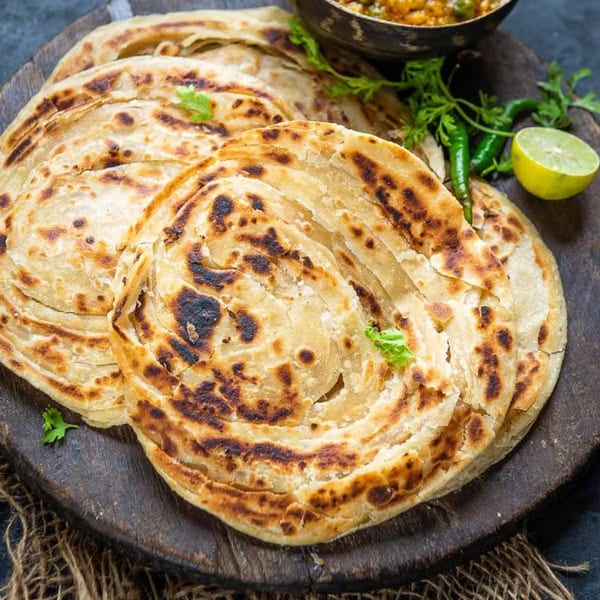 Golden-brown Indian paratha flatbreads on a wooden board, garnished with cilantro, chilies, and lime.