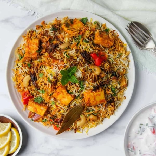 Paneer Biryani with cashews, red peppers, and mint, served with lemon slices and raita.